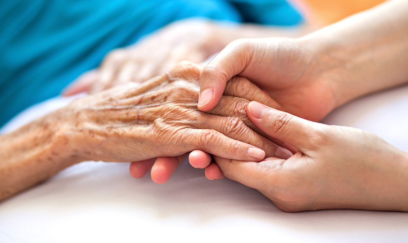 Advisacare home health caregiver holding hands of hospice client.