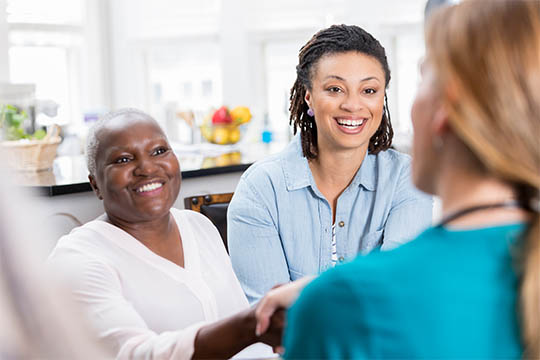 Two women smiling and engaging with a healthcare professional, representing AdvisaCare's commitment to inclusive and supportive patient care.