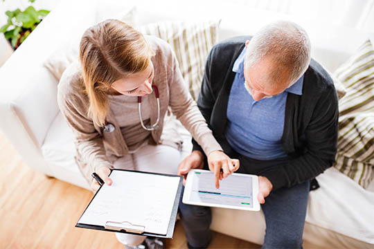 Healthcare professional reviewing care plan details with an elderly man, emphasizing AdvisaCare's personalized approach to patient care.