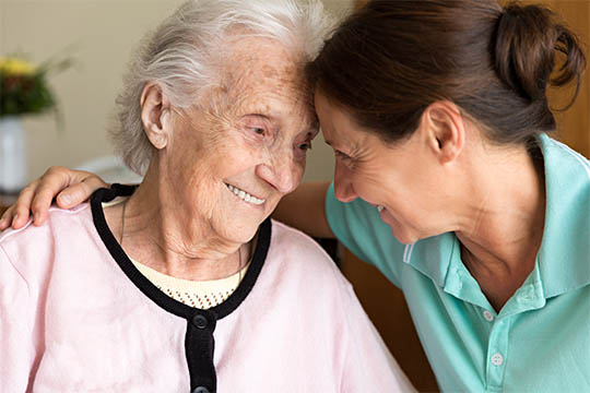 Smiling elderly woman receiving compassionate care from a caregiver, reflecting AdvisaCare's dedication to personalized and supportive care.