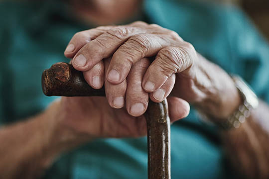 Close-up of elderly hands resting on a cane, symbolizing strength and support provided by AdvisaCare’s compassionate care services.