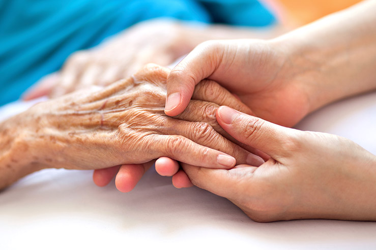 Advisacare home health aide providing comfort to a patient by holding hands during a home care visit.